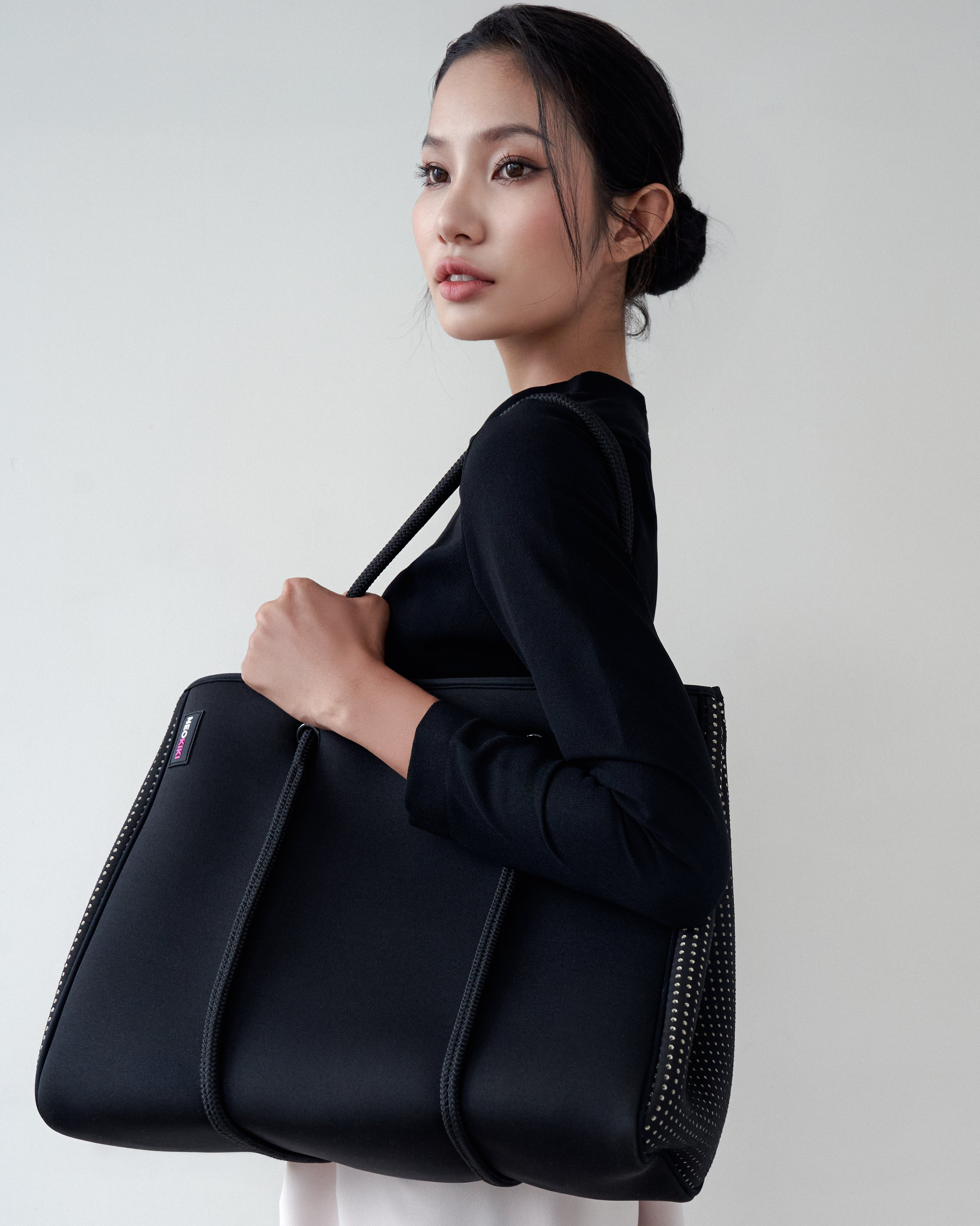 Woman holding a black handbag against a plain background